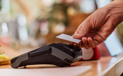 Close up of a person's hand holding a credit card up to a card reader