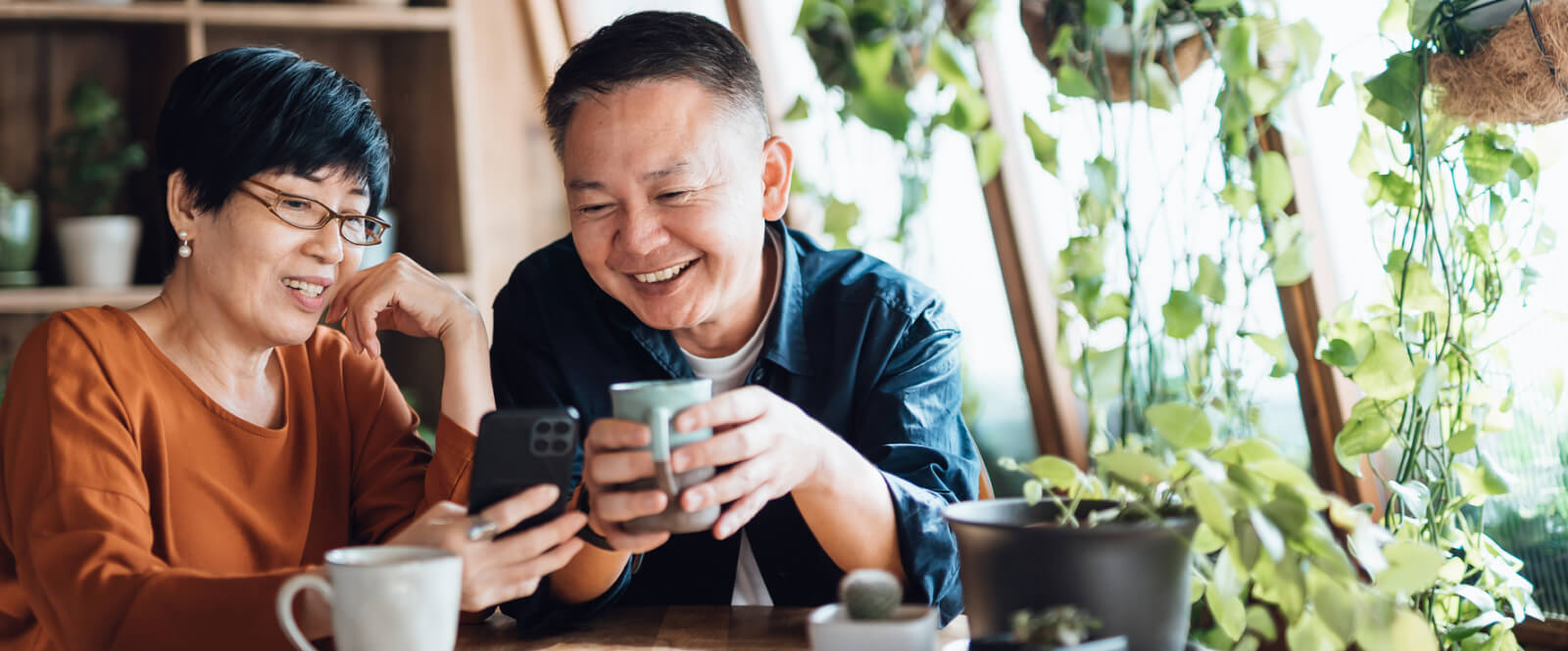 Older couple sitting with coffee and looking at a smartphone