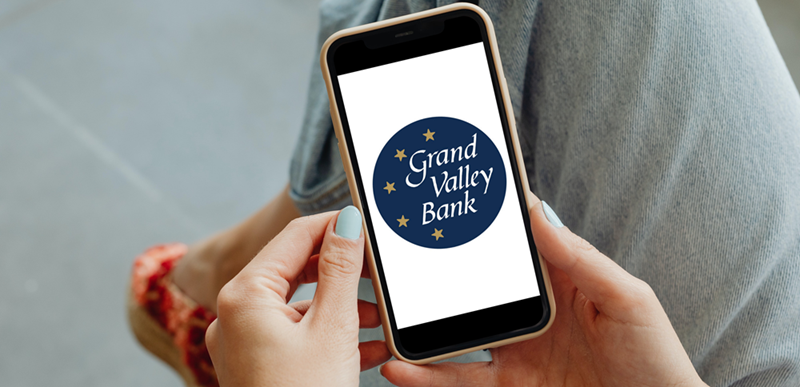 Woman holding mobile phone with Grand Valley Bank 5-Star Round Logo on mobile phone screen