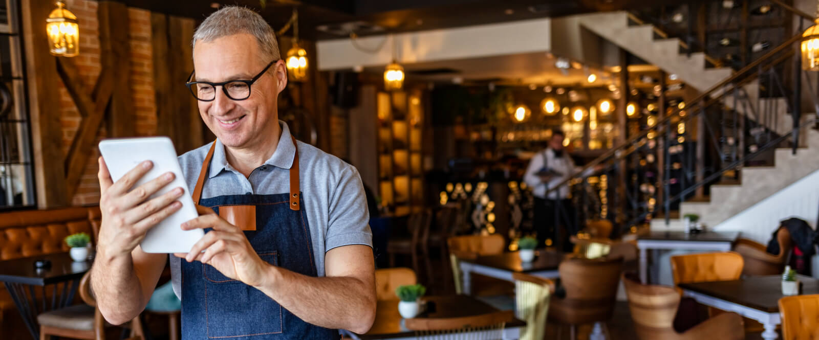Man in apron standing in a cafe holding a tablet